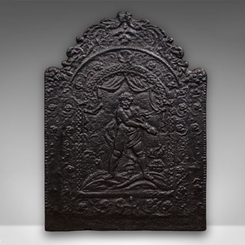 fig 1. An arched dark cast iron fireback with relief carving of a classical figure framed by scrollwork.