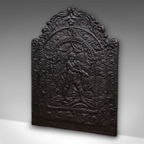 fig 2. An arched dark cast iron fireback with relief carving of a classical figure framed by scrollwork.