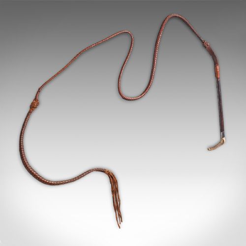 fig 1. An antique English hunting whip featuring a stag horn hook handle, silver collar band, dark shaft, and a long braided chestnut leather thong.