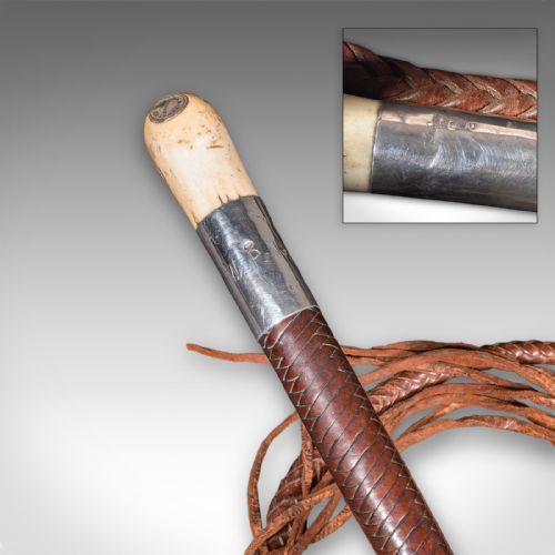 fig 3. An antique English hunting whip featuring a stag horn hook handle, silver collar band, dark shaft, and a long braided chestnut leather thong.