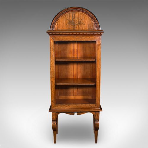 fig 1. A tall Regency oak display cabinet featuring an arched bonnet top with marquetry inlay, a single glazed door enclosing shelves, and carved front legs.