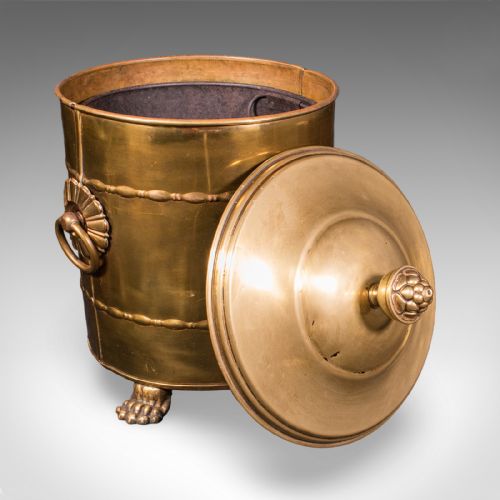 fig 1. A cylindrical brass coal bin featuring a domed lid with a finial, side ring handles, embossed scrollwork, and lion paw feet.