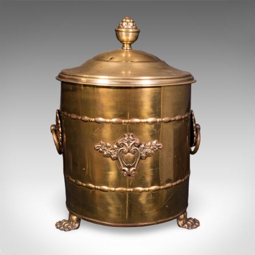 fig 3. A cylindrical brass coal bin featuring a domed lid with a finial, side ring handles, embossed scrollwork, and lion paw feet.