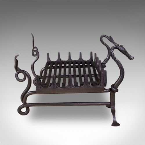 fig 2. A black hand-forged wrought iron fire basket featuring a curved slatted grate supported by four legs with dragon head and tail terminals.
