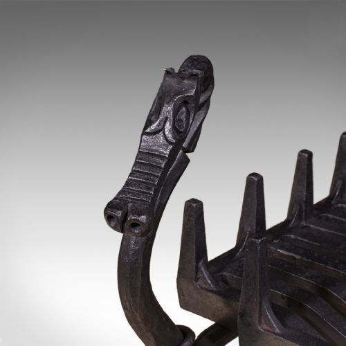 fig 4. A black hand-forged wrought iron fire basket featuring a curved slatted grate supported by four legs with dragon head and tail terminals.