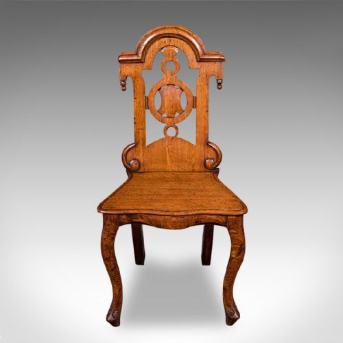 fig 1. A carved Scottish Victorian oak hall chair featuring a decorative pierced backrest, a solid shaped seat, cabriole front legs, and splayed rear legs.