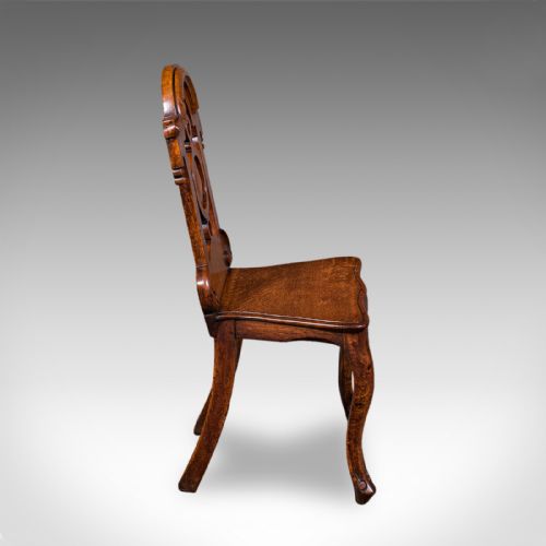 fig 2. A carved Scottish Victorian oak hall chair featuring a decorative pierced backrest, a solid shaped seat, cabriole front legs, and splayed rear legs.