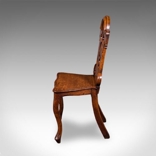 fig 4. A carved Scottish Victorian oak hall chair featuring a decorative pierced backrest, a solid shaped seat, cabriole front legs, and splayed rear legs.