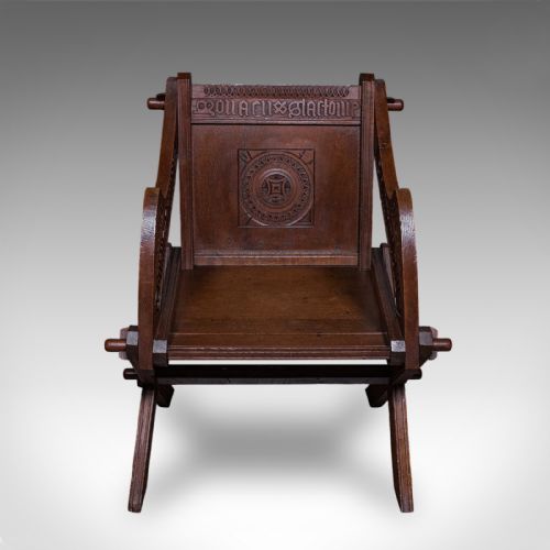 fig 1. A dark oak Glastonbury chair featuring an X-frame structure with wooden pegs, carved Latin inscriptions on the arms, and a carved backrest panel.
