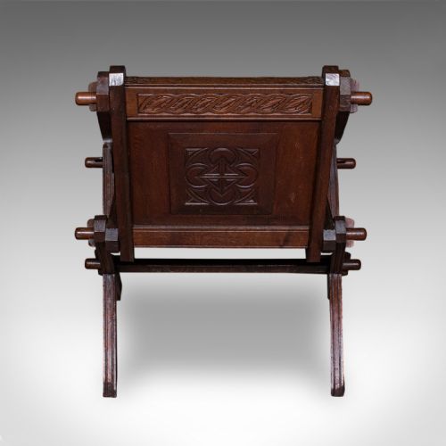 fig 3. A dark oak Glastonbury chair featuring an X-frame structure with wooden pegs, carved Latin inscriptions on the arms, and a carved backrest panel.