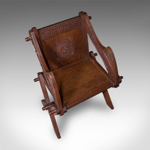 fig 5. A dark oak Glastonbury chair featuring an X-frame structure with wooden pegs, carved Latin inscriptions on the arms, and a carved backrest panel.