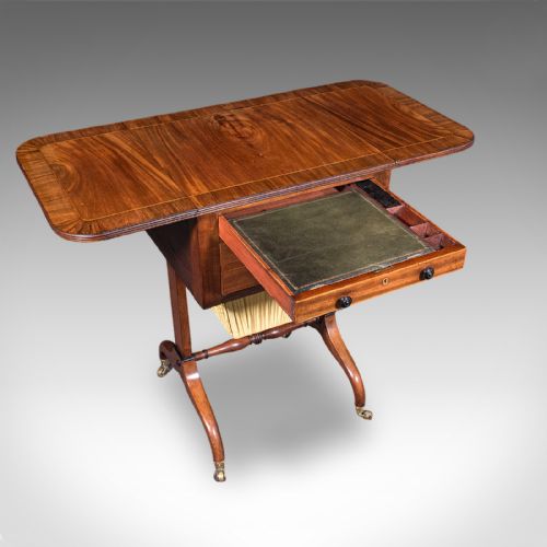 fig 1. A Regency mahogany drop-leaf sewing table with three drawers, a pleated cream fabric work basket, and swept legs on brass castors.
