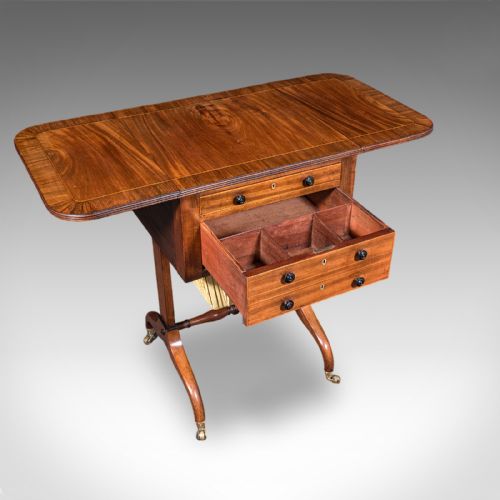 fig 3. A Regency mahogany drop-leaf sewing table with three drawers, a pleated cream fabric work basket, and swept legs on brass castors.