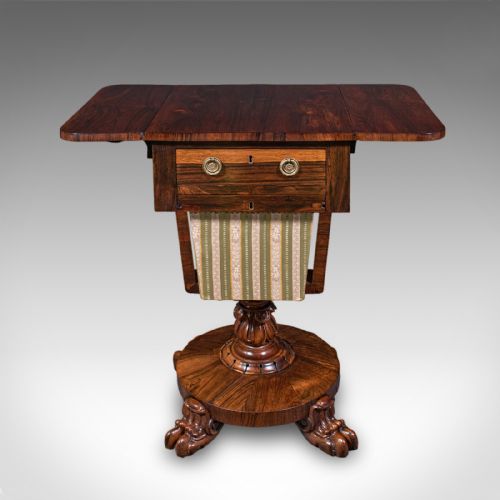fig 3. A William IV dark rosewood drop-leaf sewing table featuring a top drawer, a fabric work basket below, and a carved pedestal base with paw feet.