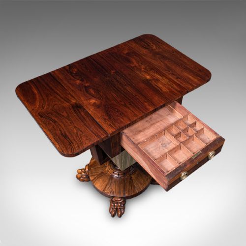 fig 6. A William IV dark rosewood drop-leaf sewing table featuring a top drawer, a fabric work basket below, and a carved pedestal base with paw feet.