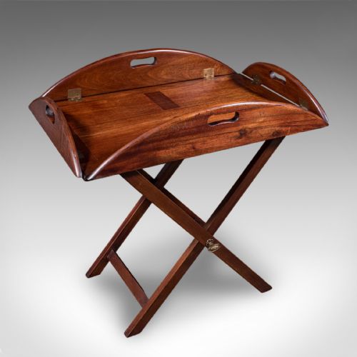 fig 1. An Edwardian mahogany butlers tray table featuring an oval top with fold-down flaps, brass flush hinges, cut-out carrying handles, and a folding X-frame base.