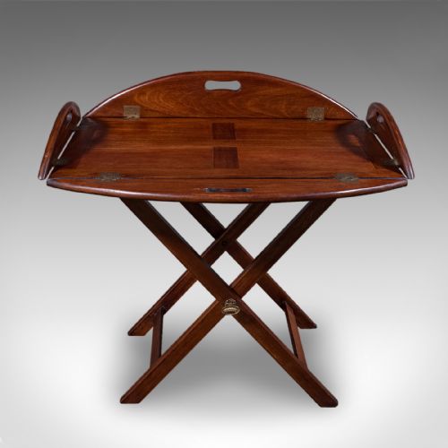 fig 3. An Edwardian mahogany butlers tray table featuring an oval top with fold-down flaps, brass flush hinges, cut-out carrying handles, and a folding X-frame base.
