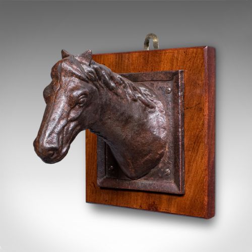 fig 2. A cast iron horse head bust mounted within an iron frame on a square polished wooden plaque.