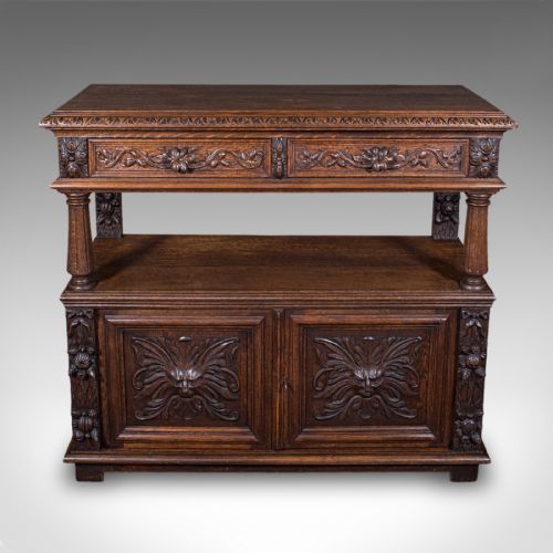 fig 2. A dark Victorian carved oak buffet sideboard featuring a two-tier structure, turned support pillars, carved frieze drawers, and lower cupboard doors decorated with relief carvings of grotesque mask motifs.