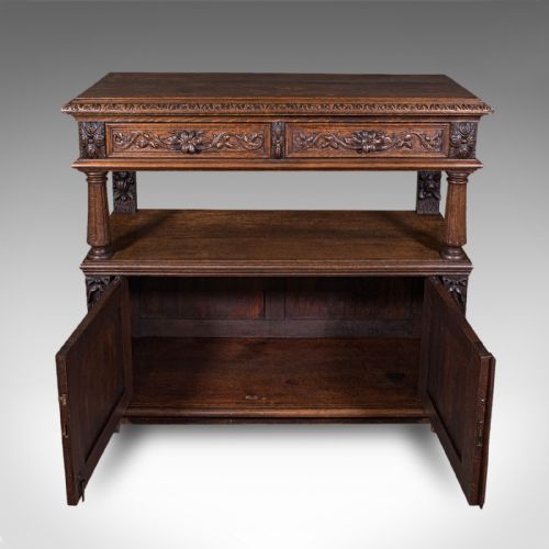 fig 3. A dark Victorian carved oak buffet sideboard featuring a two-tier structure, turned support pillars, carved frieze drawers, and lower cupboard doors decorated with relief carvings of grotesque mask motifs.