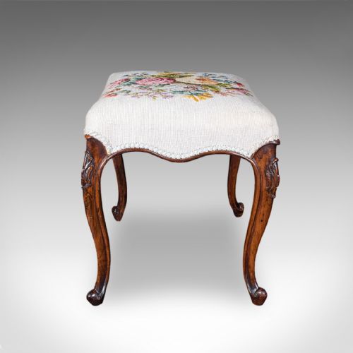 fig 2. An Early Victorian walnut footstool featuring cabriole legs and a cream upholstered top detailed with a floral needlepoint design.