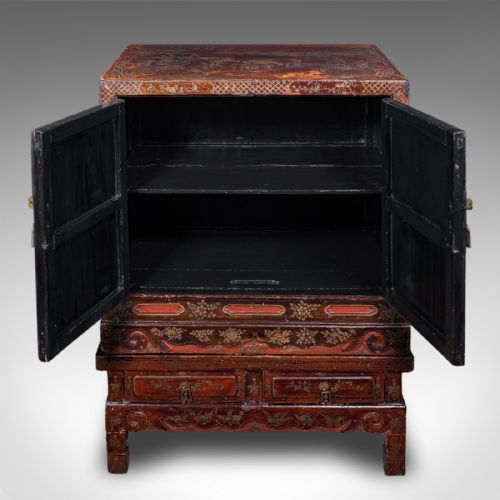 fig 1. An antique reddish-brown lacquered Chinoiserie campaign cabinet featuring gold gilt landscape scenes, brass corner mounts, and two open lower drawers on a matching stand.