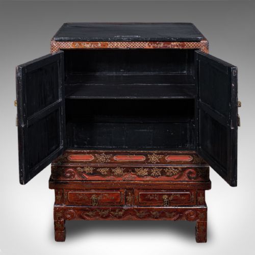 fig 2. An antique reddish-brown lacquered Chinoiserie campaign cabinet featuring gold gilt landscape scenes, brass corner mounts, and two open lower drawers on a matching stand.