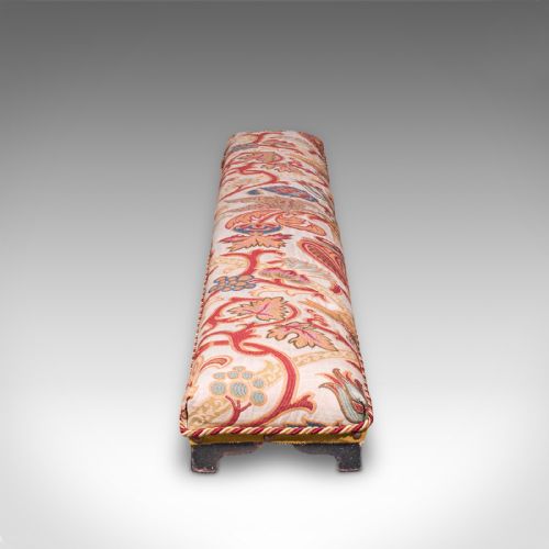 fig 2. An elongated Victorian carriage stool featuring multicoloured crewelwork floral upholstery with braid trim and short turned dark wooden legs.