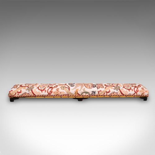 fig 3. An elongated Victorian carriage stool featuring multicoloured crewelwork floral upholstery with braid trim and short turned dark wooden legs.