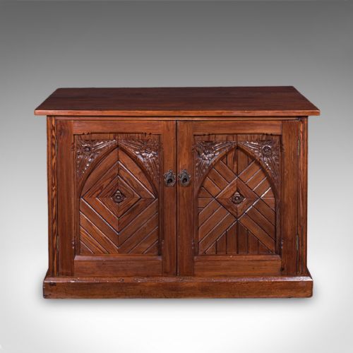 fig 1. A low Victorian Gothic Revival wooden cabinet with double doors featuring carved pointed arches, geometric panelling, and twin metal drop handles.
