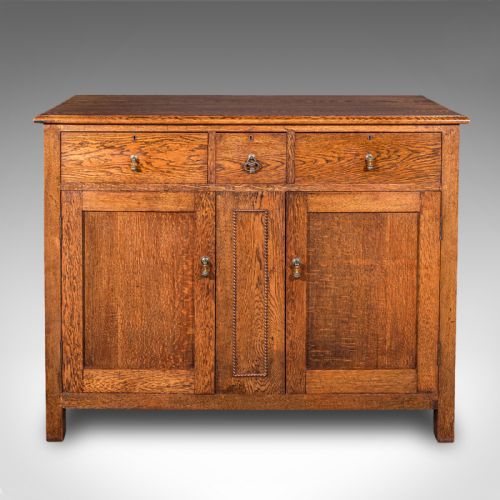 fig 1. An antique Edwardian medium brown oak sideboard featuring three upper drawers with brass drop handles above panelled cupboard doors.