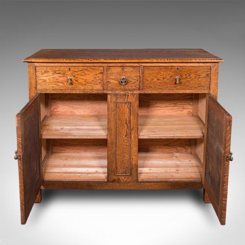 fig 2. An antique Edwardian medium brown oak sideboard featuring three upper drawers with brass drop handles above panelled cupboard doors.