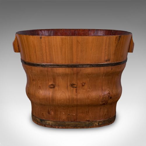 fig 1. An oval late Victorian Dutch cedar waste paper basket with brass binding straps and carved side handles on a light background.