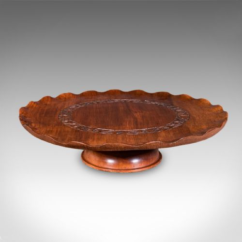 fig 1. A circular carved wooden lazy susan featuring a scalloped outer border, a central carved foliate ring, and a revolving pedestal base.