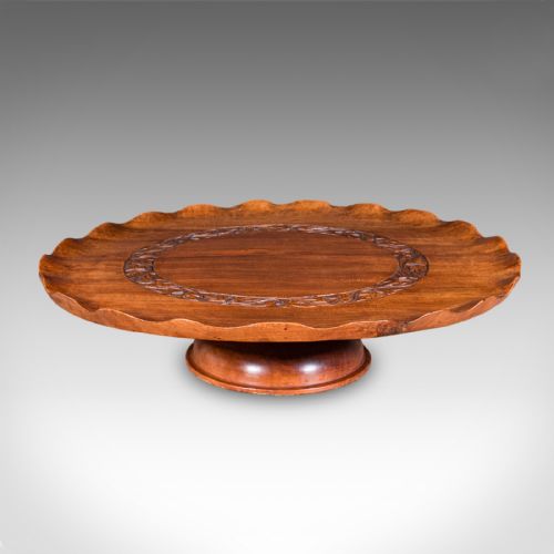 fig 2. A circular carved wooden lazy susan featuring a scalloped outer border, a central carved foliate ring, and a revolving pedestal base.
