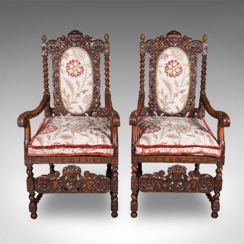fig 2. A pair of carved dark oak armchairs featuring barley twist uprights, intricate cherub carvings, and cream floral tapestry upholstery with red fringe trim.