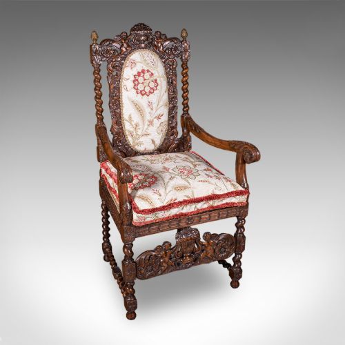 fig 3. A pair of carved dark oak armchairs featuring barley twist uprights, intricate cherub carvings, and cream floral tapestry upholstery with red fringe trim.