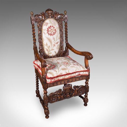fig 4. A pair of carved dark oak armchairs featuring barley twist uprights, intricate cherub carvings, and cream floral tapestry upholstery with red fringe trim.