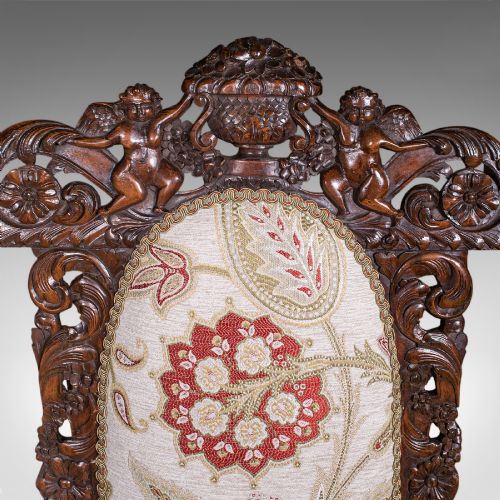 fig 5. A pair of carved dark oak armchairs featuring barley twist uprights, intricate cherub carvings, and cream floral tapestry upholstery with red fringe trim.