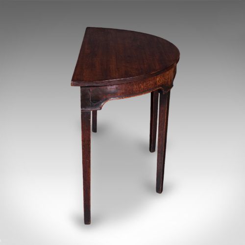 fig 2. An antique dark mahogany demi-lune console table featuring tapered legs and a curved frieze.