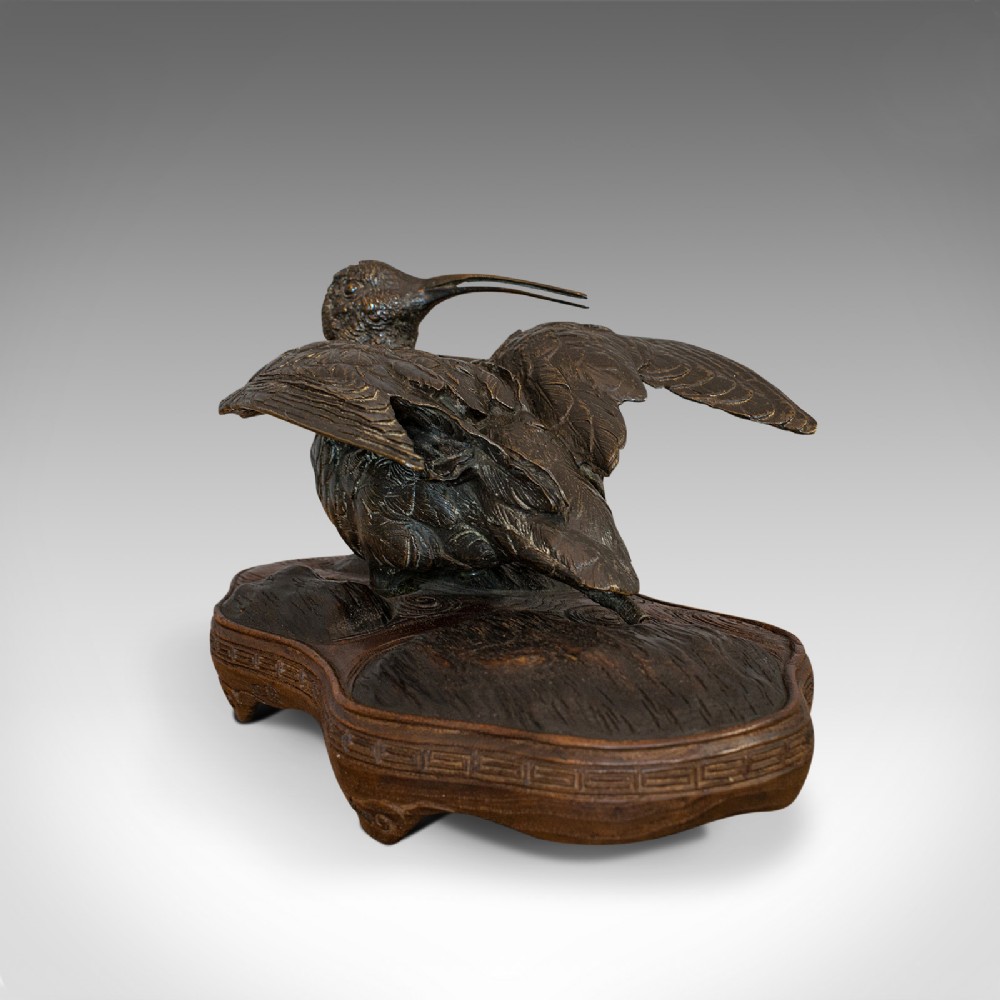 An antique bronze sculpture depicting a curlew bird with outstretched wings, set upon a carved mahogany base.