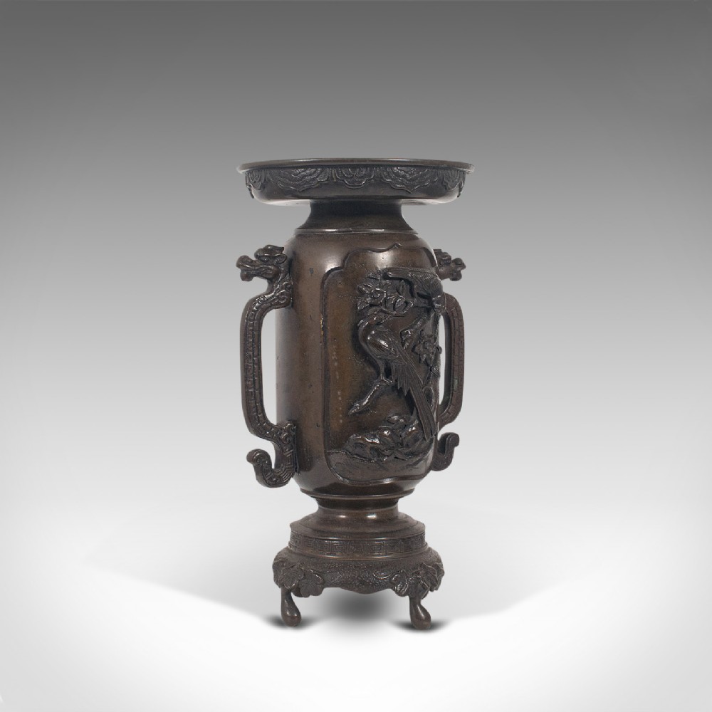 A dark brown bronze Japanese Meiji period vase featuring relief carving of a bird on a branch, ornate handles, and a pedestal base.