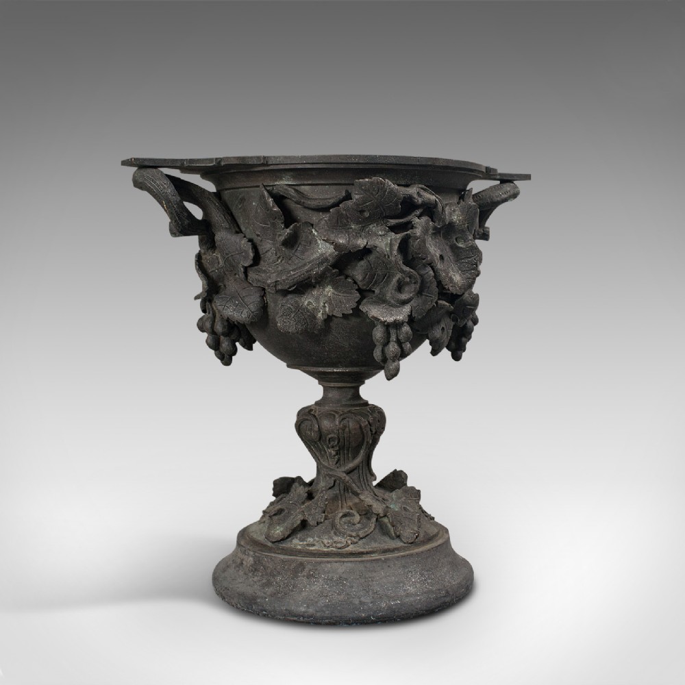 An 18th-century Continental dark bronze serving cup featuring detailed grapevine relief carving, twin side handles, and a flared pedestal base.