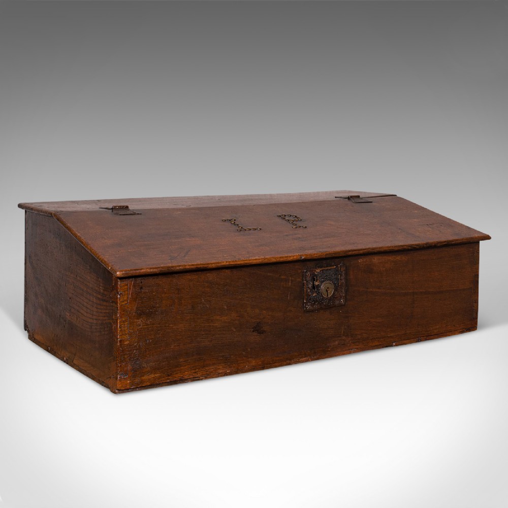 A dark brown antique oak tabletop writing desk featuring a sloped hinged lid with studded initials and a metal front lockplate.