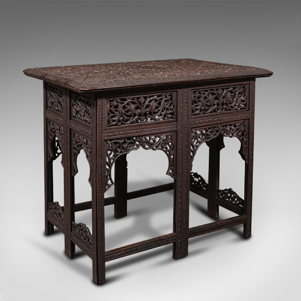A dark brown carved teak folding occasional table featuring intricate floral openwork panels and arches.