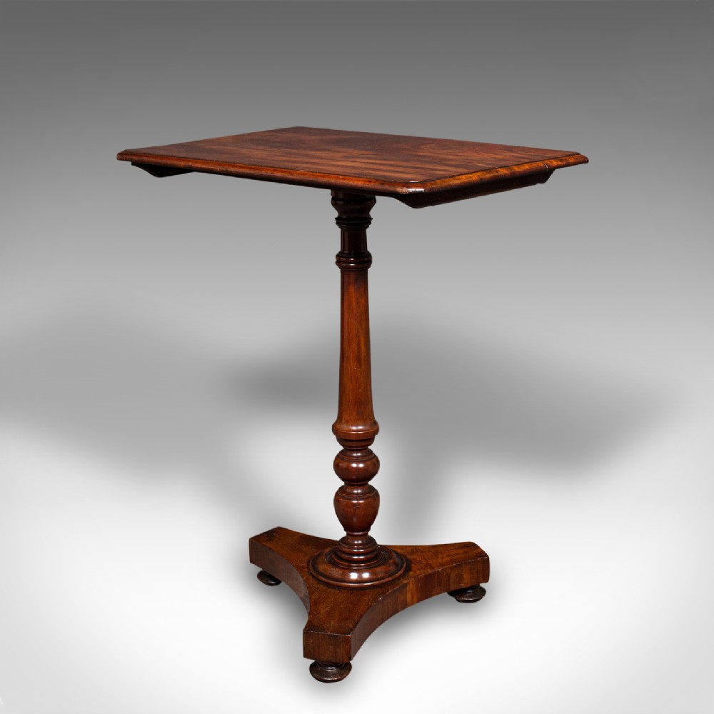 A Regency flame mahogany tilting lamp table featuring a rectangular top, turned pedestal stem, and tri-form base.