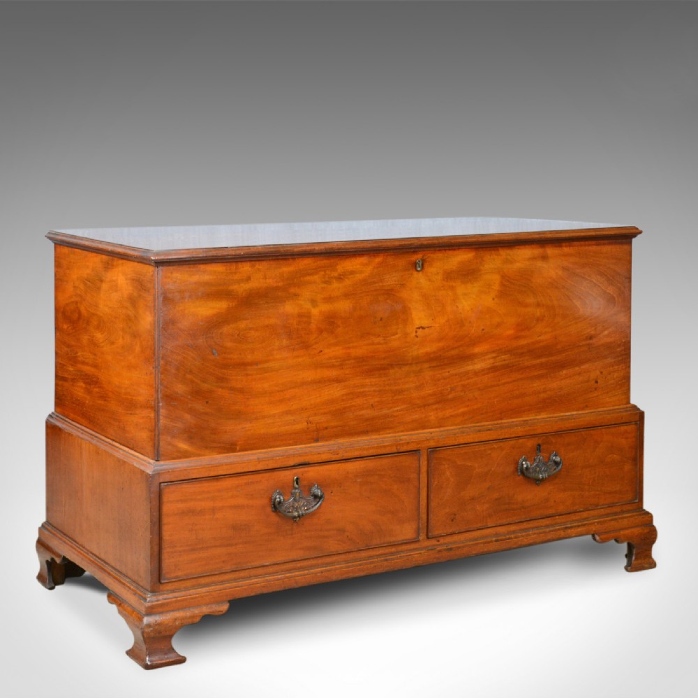A Georgian mahogany mule chest featuring a hinged top lid, two lower drawers with brass drop handles, resting on bracket feet.
