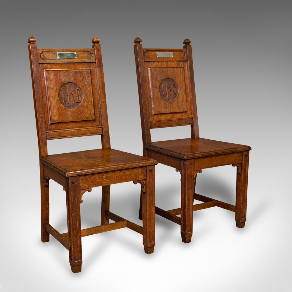 A pair of antique Victorian English oak hall chairs featuring carved IHS monograms on the backrests and solid wooden seats.