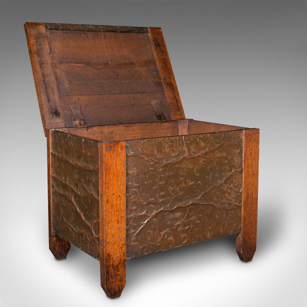 An Edwardian oak coal keeper featuring an open hinged lid and textured hammered copper panels mounted within a solid wooden frame.