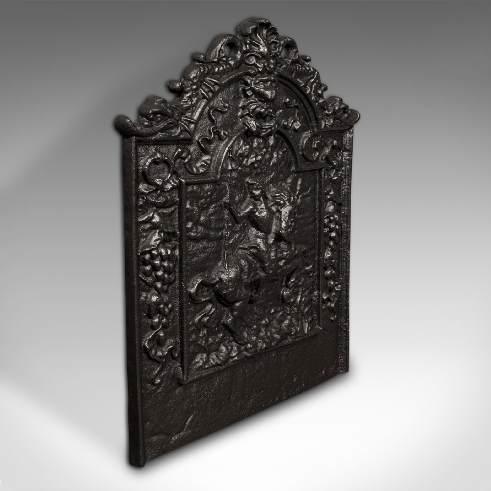 A dark cast iron Georgian fireback decorated with an equestrian relief figure surrounded by detailed foliate and scroll cresting.